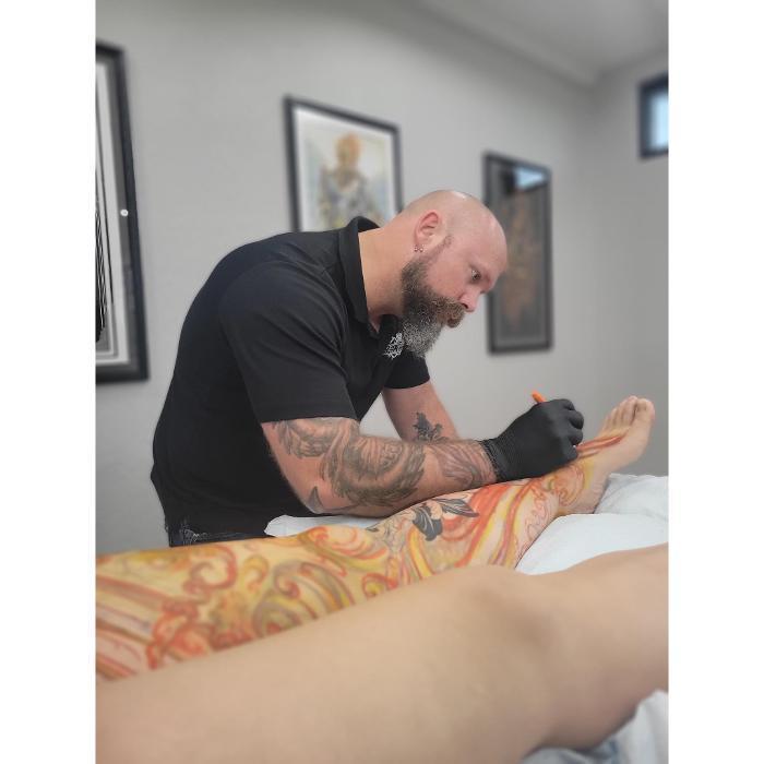 Tattoo artist Cory working on a custom leg sleeve at Red Arbor Tattoo in Tea, South Dakota.