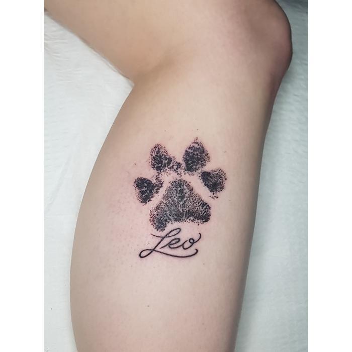Pet memorial tattoo with paw print and name. Small, meaningful tribute done in fine line and script lettering.