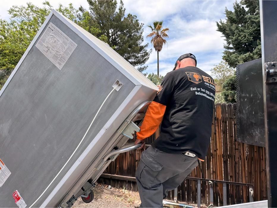 Bella Junk Removal crew member hauling a refrigerator on a hand truck during an appliance removal job.