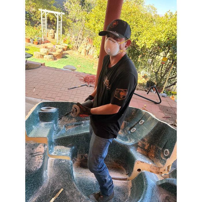 William using a reciprocating saw to saw a hot tub in half for removal.