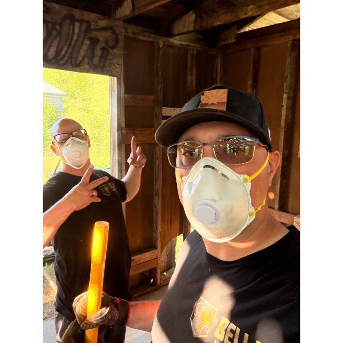 Bella Junk Removal crew wearing protective masks while cleaning out a dusty shed during a cleanout job.