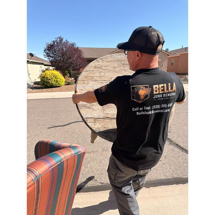 Bella Junk Removal crew member carrying a table to the dump trailer during a junk removal job in the Verde Valley.