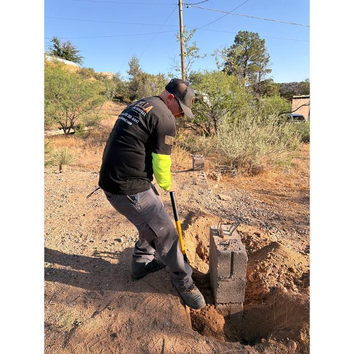 Robert digging up a concrete block pier using a shovel.
