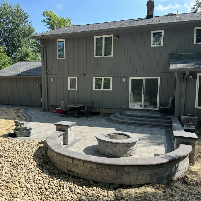 Get ready for bonfire nights! This expansive paver patio is designed for entertaining, featuring a custom built-in fire pit with a curved seating wall. From the river rock drainage details to the seamless steps, every inch is built for hosting.