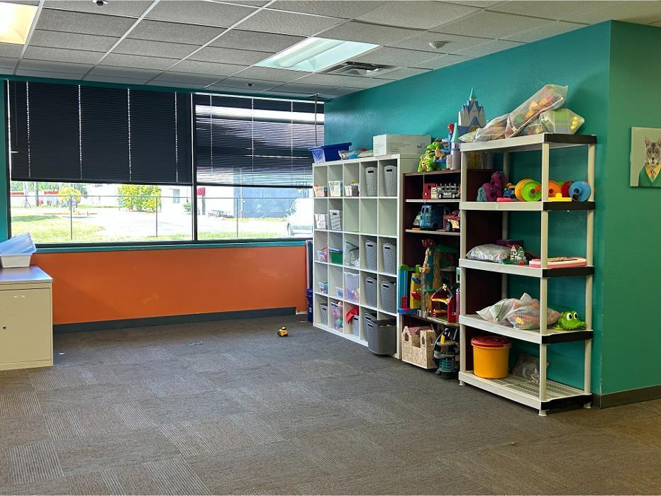 Organized storage area in a therapy room featuring white cubbies and shelving filled with educational toys, games, and learning materials for Applied Behavior Analysis (ABA) sessions.