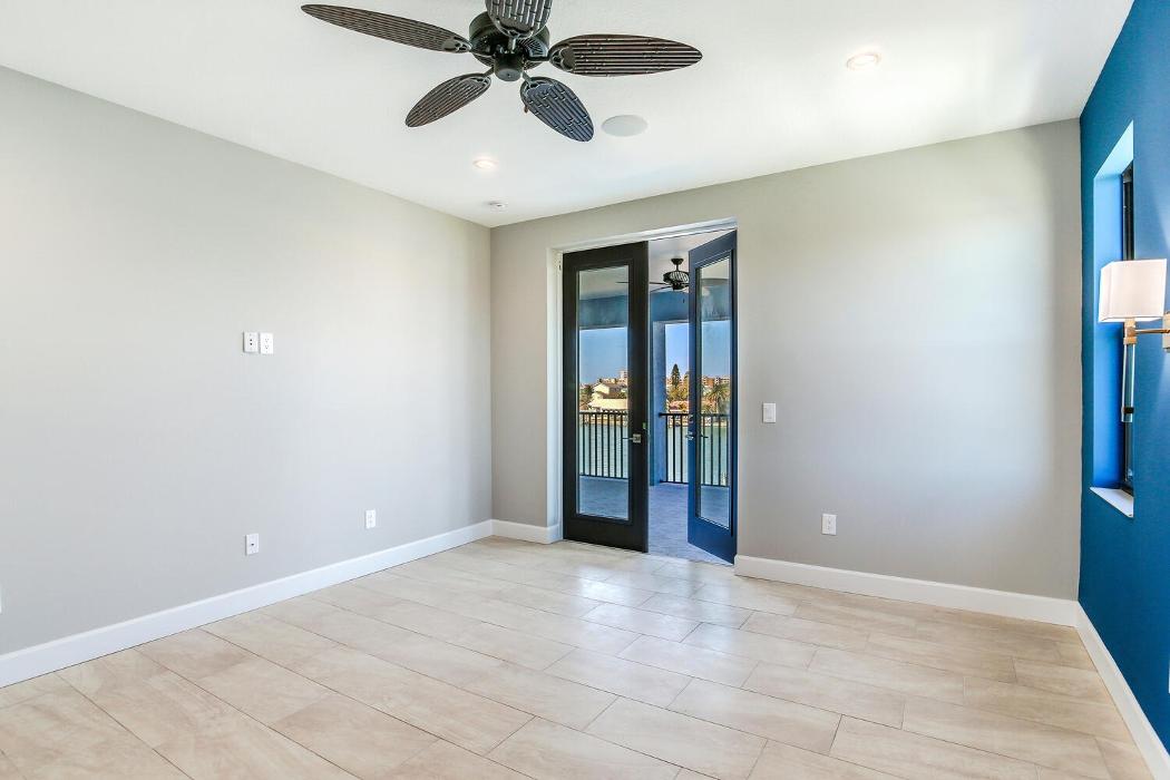 Bright bedroom with light wood-look flooring, gray walls, a ceiling fan, and glass doors leading to a balcony.