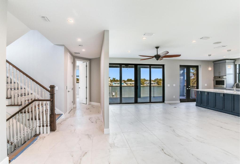 Bright open-concept interior featuring a modern staircase with wood and metal railing, light tile flooring, recessed lighting, and a spacious living area connected to the kitchen.