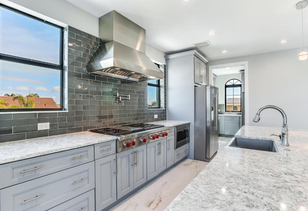 Modern kitchen with gray upper cabinetry, blue lower cabinets, stainless steel appliances, a large window, and light wood-look flooring.