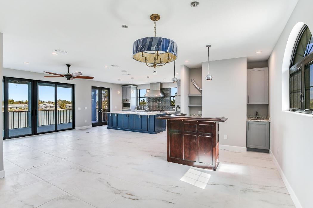 Spacious open living and kitchen area with glossy tile flooring, a large island with blue cabinetry, pendant lighting, and expansive windows.