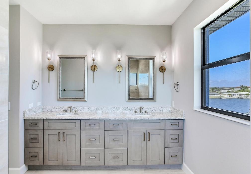 Modern bathroom vanity with dual sinks, gray cabinetry, wall sconces, and a large window bringing in natural light.