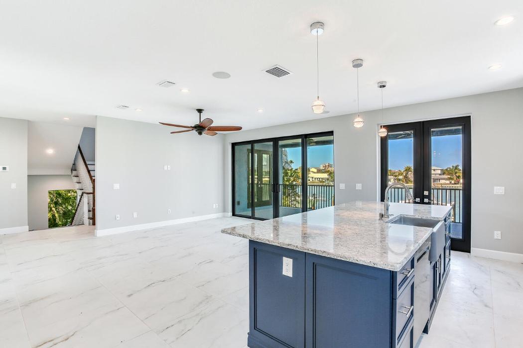 Spacious modern kitchen with a blue island, light countertops, recessed lighting, and an open layout flowing into the living area.