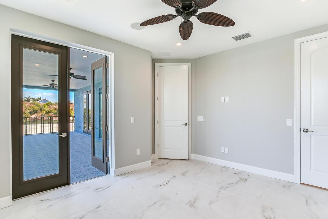 Bright bedroom with light flooring, soft gray walls, a ceiling fan, and glass doors opening to a balcony or outdoor area.