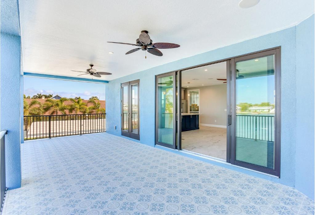 Covered outdoor living space with blue tile flooring, a ceiling fan, sliding glass doors, and an open layout overlooking the exterior.