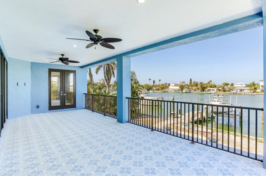 Covered waterfront balcony with blue tile flooring, a ceiling fan, black railing, and expansive water views.