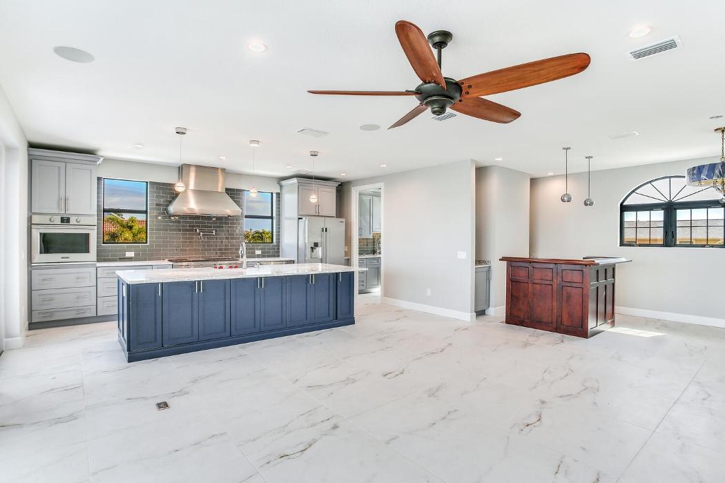 Spacious open-concept living and kitchen area with light flooring, a large ceiling fan, blue island cabinetry, and a bright, airy design.