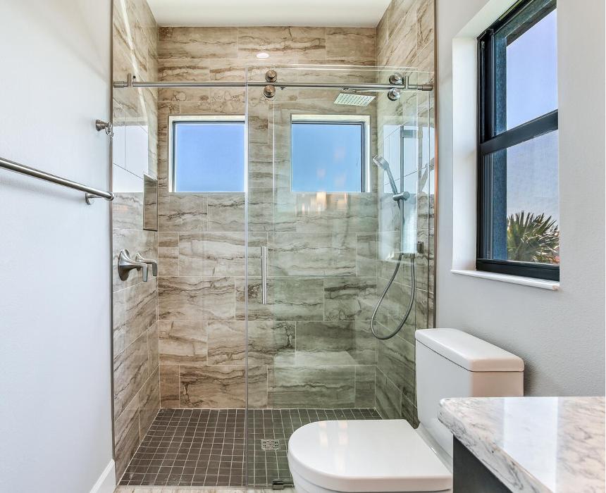 Modern bathroom with a glass-enclosed shower, stone-look tile walls, a toilet, and a large window for natural light.