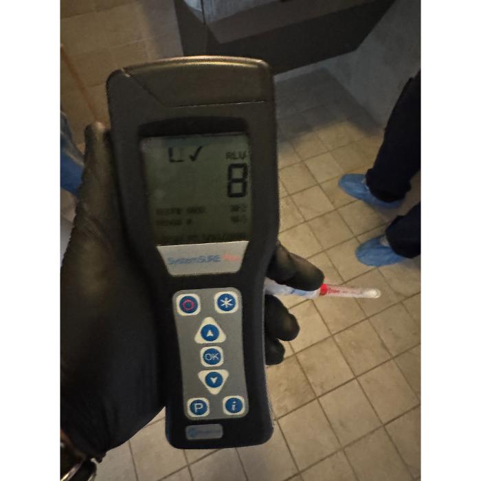 A close-up of a handheld digital inspection meter displaying a reading while being used inside an indoor space.