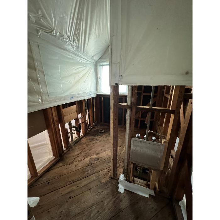 An unfinished room or basement section with exposed wall framing and plastic containment sheeting hanging from the ceiling.
