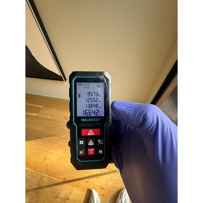 A close-up of a handheld moisture meter or inspection device being held up near a ceiling or wall surface.