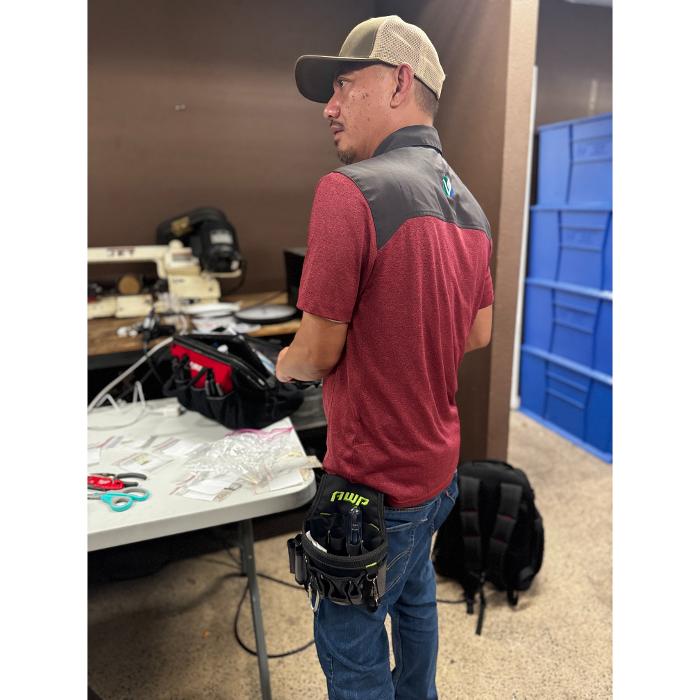 A technician standing beside a table of tools and equipment, appearing to prepare or review materials in an indoor work area.