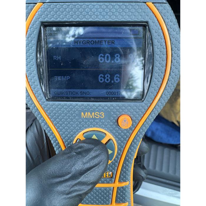 A close-up of a handheld digital moisture meter showing a reading while being used on a surface.