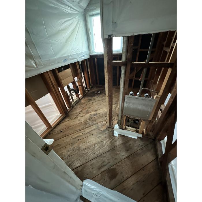 Another angle of the same unfinished contained area, showing exposed studs, open flooring, and restoration equipment positioned near the wall.