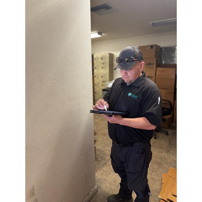 A technician standing in a hallway or interior room, holding a device or clipboard while documenting or inspecting the area.