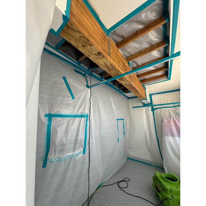 Another view of the same contained space, showing plastic-covered walls, exposed framing, and a green air scrubber or equipment unit on the floor.