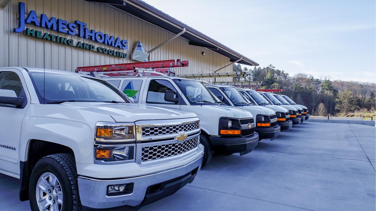 Line of branded service trucks parked outside the company building, ready for HVAC service calls.