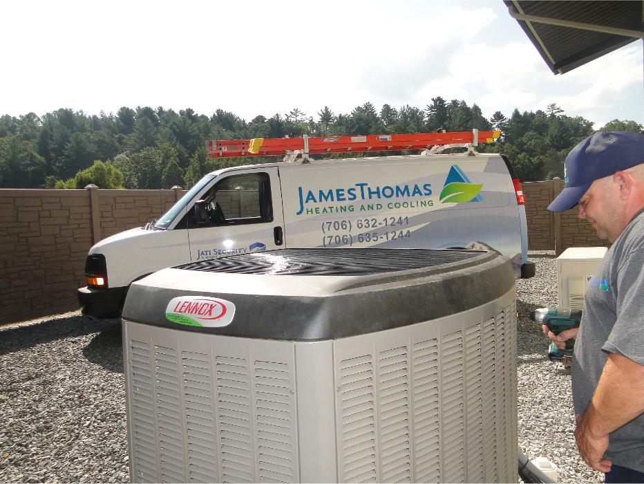 Technician working beside an outdoor HVAC unit with a branded service van parked nearby.