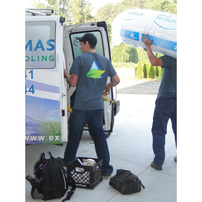 HVAC technicians standing beside a branded service van while preparing equipment for an on-site service call.