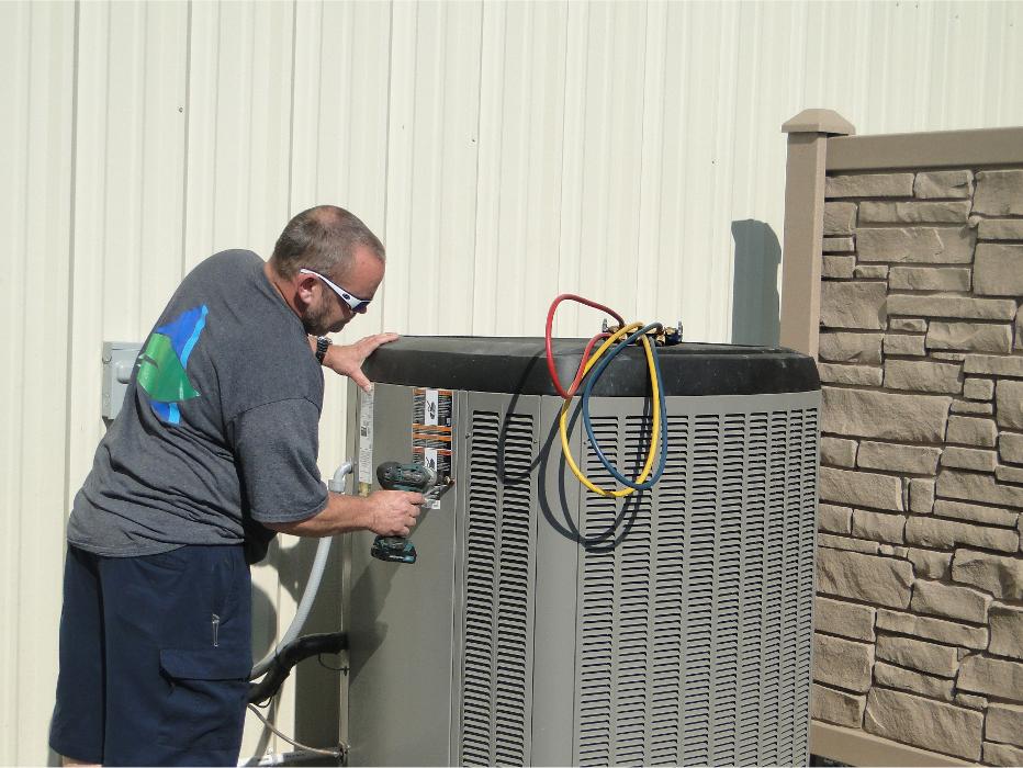 HVAC technician servicing an outdoor air conditioning unit beside a home.