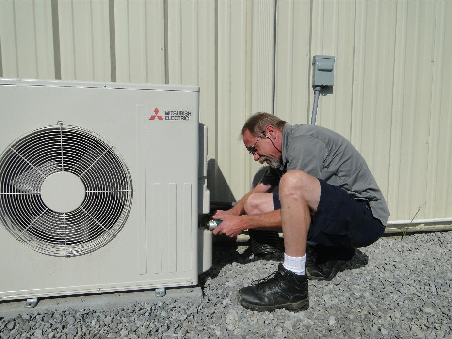 Technician working on a ductless mini-split system installation outside a building.