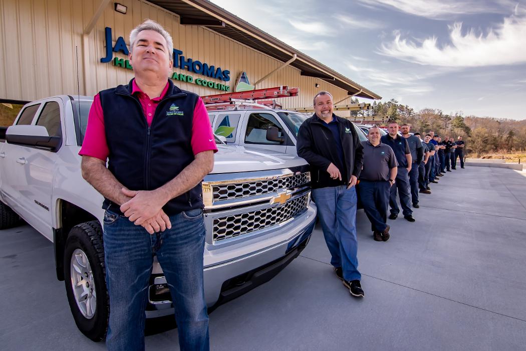 Team members standing in front of branded service trucks outside a commercial building, showcasing company staff and vehicles.