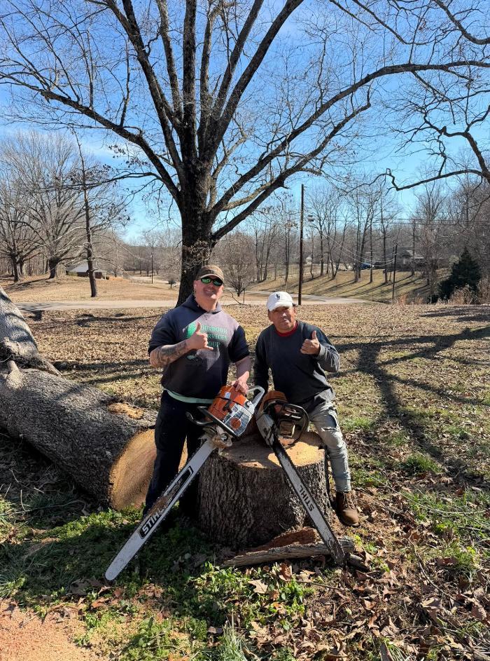 Two Outdoor Services Group crew members posing beside a freshly cut tree and stump during a tree removal project.