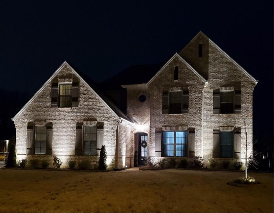 Front exterior of a home illuminated by professionally installed landscape lighting at night.