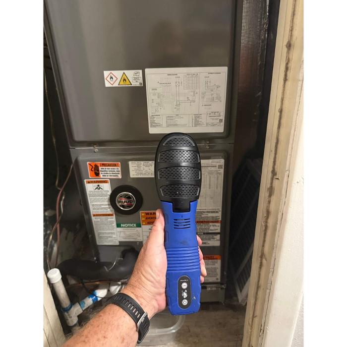 Technician using a handheld inspection device near an electrical or utility panel to evaluate indoor environmental conditions and possible moisture issues.