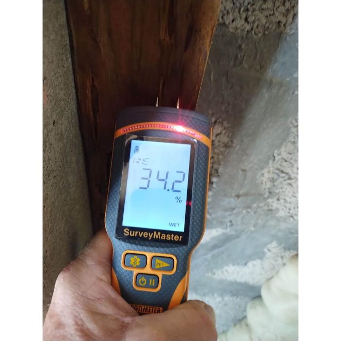 A handheld moisture meter is being used to measure elevated moisture levels in a building material during an inspection.