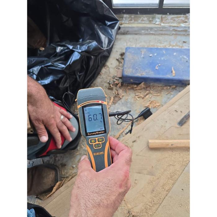 A technician using a handheld moisture meter during an indoor environmental inspection to detect hidden moisture in building materials.