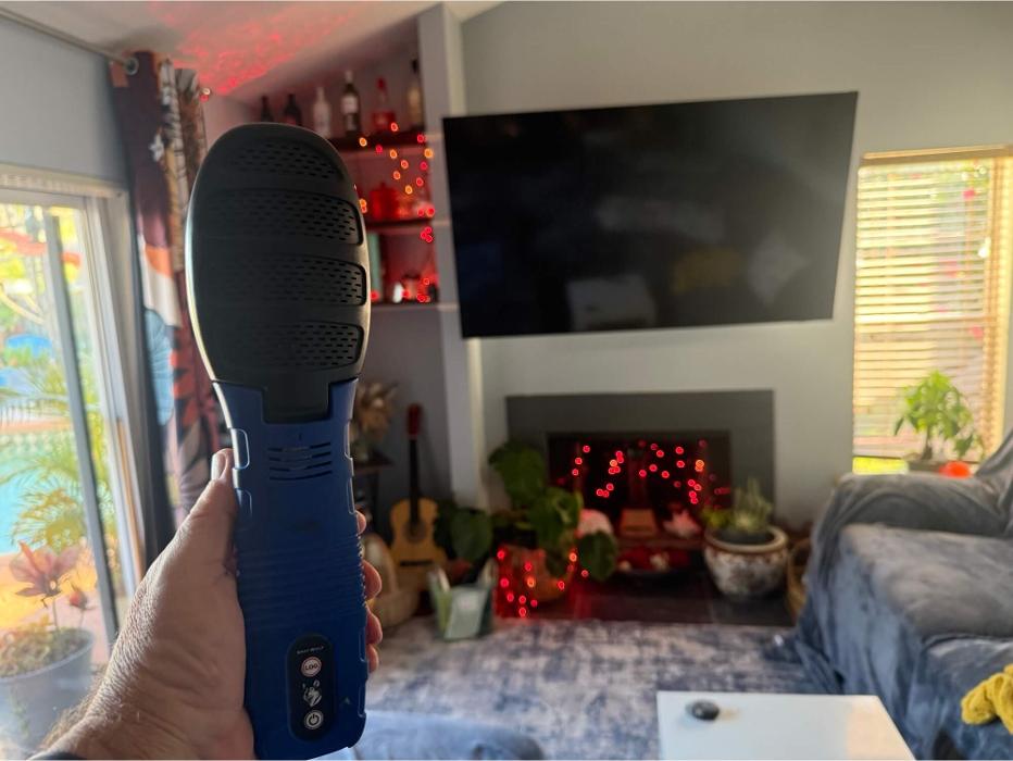 Technician using a handheld indoor environmental testing device inside a living room to assess air quality and building health conditions.