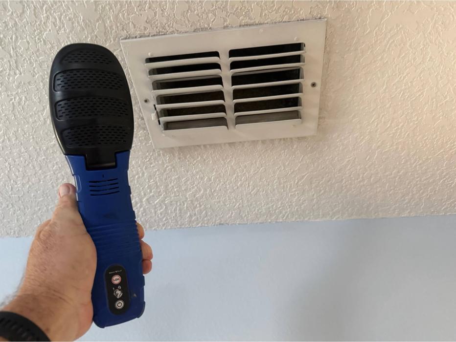 A technician using a handheld inspection device to test airflow or conditions at an HVAC vent during an indoor environmental assessment.