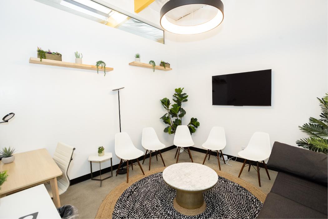 A welcoming group therapy room equipped with cozy, curved seating, a modern patterned rug, and a television, creating an inviting space for adolescent outpatient sessions.