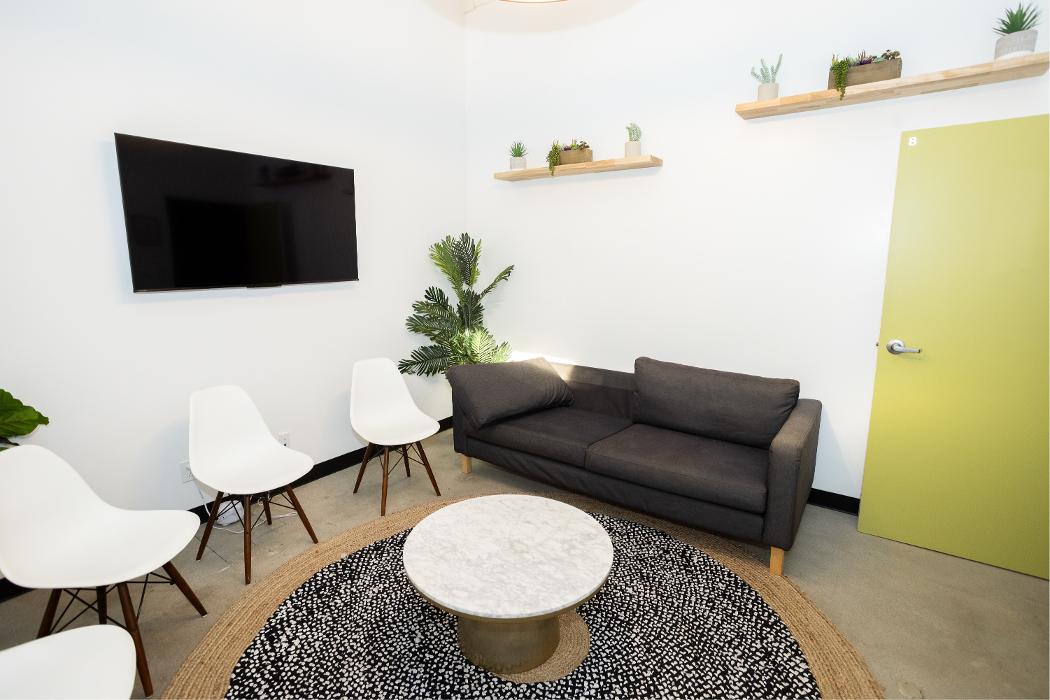 A modern teen lounge highlighting a vibrant green accent wall, comfortable seating, and a television, perfect for relaxation and downtime between therapeutic activities at Key Healthcare.