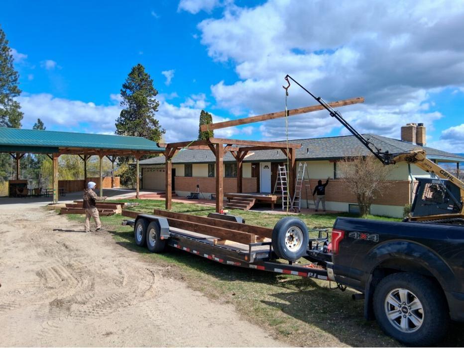 Custom timber pavilion installation in progress with heavy equipment and crane lifting large timber beams onto a residential home in Montana. Western Timber Structures is building a heavy timber-covered patio and outdoor living structure