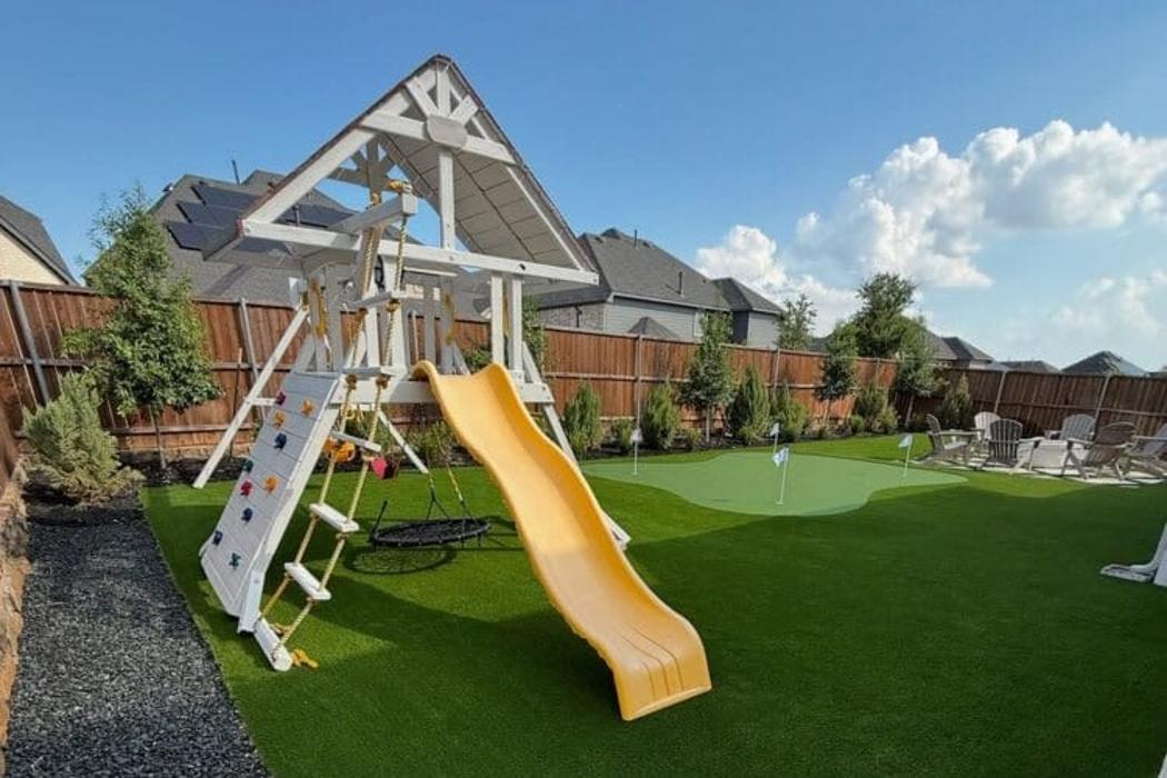 Artificial turf backyard with playset, putting green, and seating area.