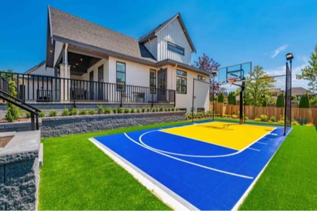 Backyard basketball court with bright blue and yellow surface and artificial turf.
