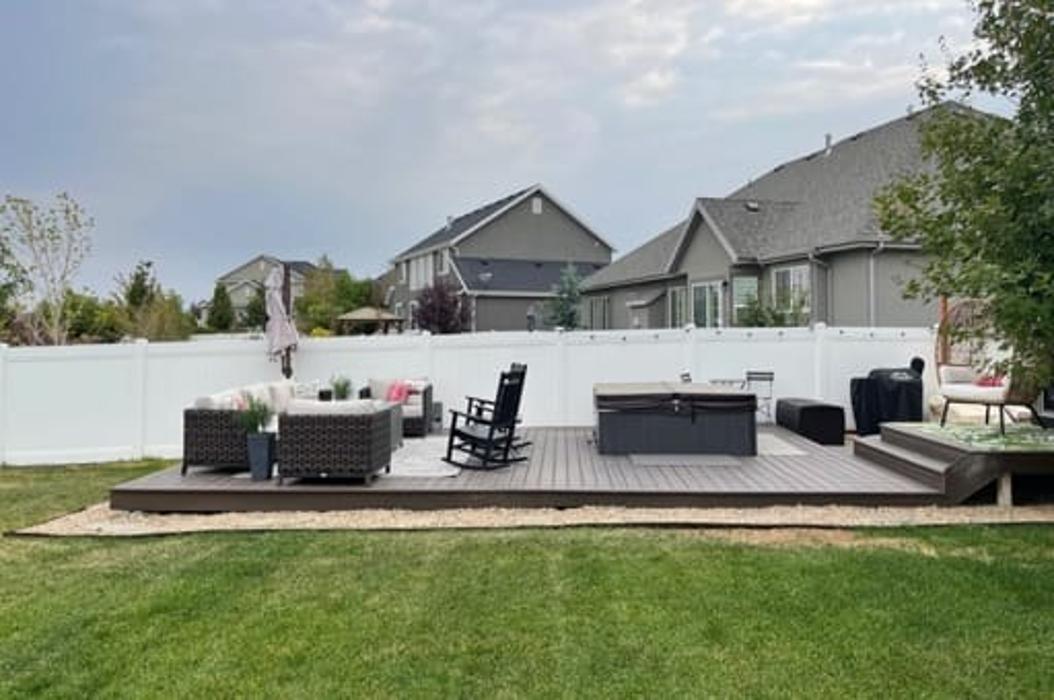 Low composite deck with hot tub and outdoor seating in a fenced backyard.