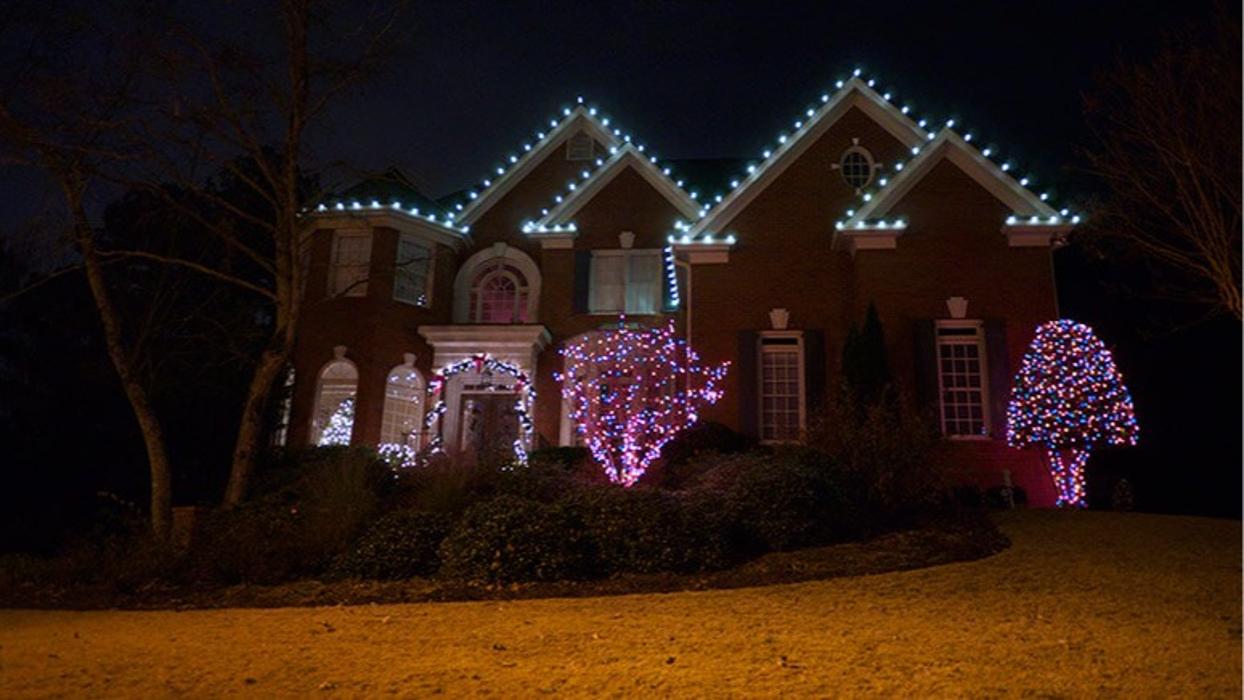 A home adorned with custom holiday lighting, including roofline lights, illuminated trees, and glowing landscape accents at night.