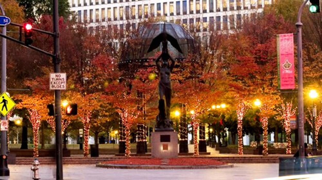 A beautifully decorated outdoor plaza featuring glowing holiday lights, illuminated trees, and festive seasonal displays in a city setting.