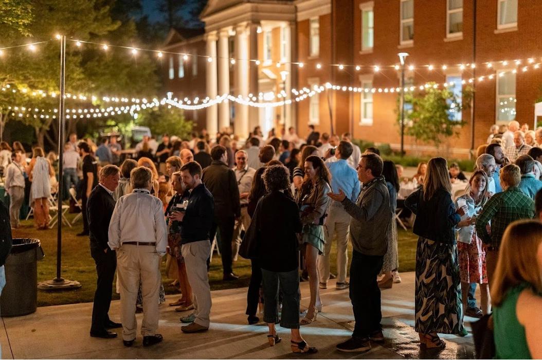 Guests gathered beneath caf&eacute; lights in a beautifully lit outdoor space, showcasing custom event lighting for an upscale evening experience.